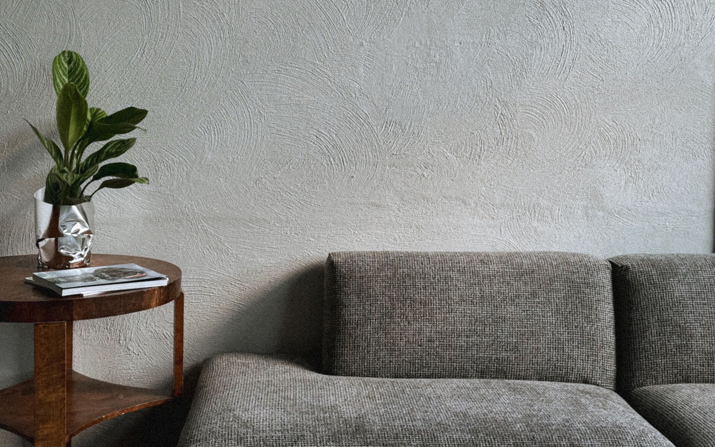 Premium minimalist living room with textured plaster wall, styled wood console, plant and linen sofa